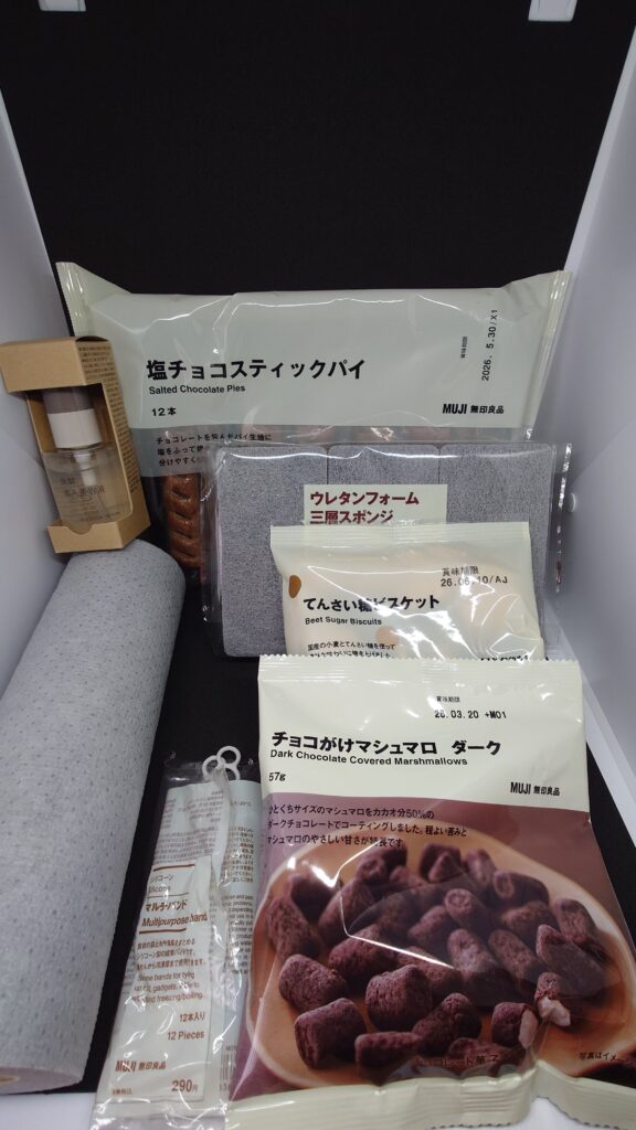 無印良品週間の人気商品TOP10を並べた写真。塩チョコスティックパイ、ウレタンフォーム三層スポンジ、てんさい糖ビスケット、チョコがけマシュマロなどの無印良品アイテムが正面に配置されている。