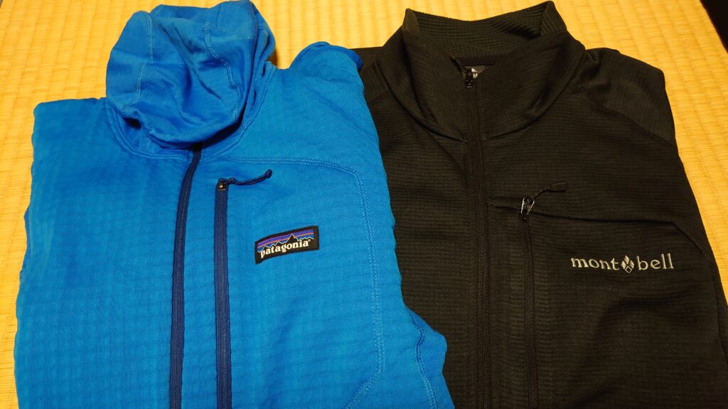 パタゴニア R1 プルオーバー・フーディ（青）と、モンベル クリマグリッド ジャケット（黒）が並べて置かれている画像。グリッドフリースの生地感と胸ポケットの位置、ロゴが確認できる。