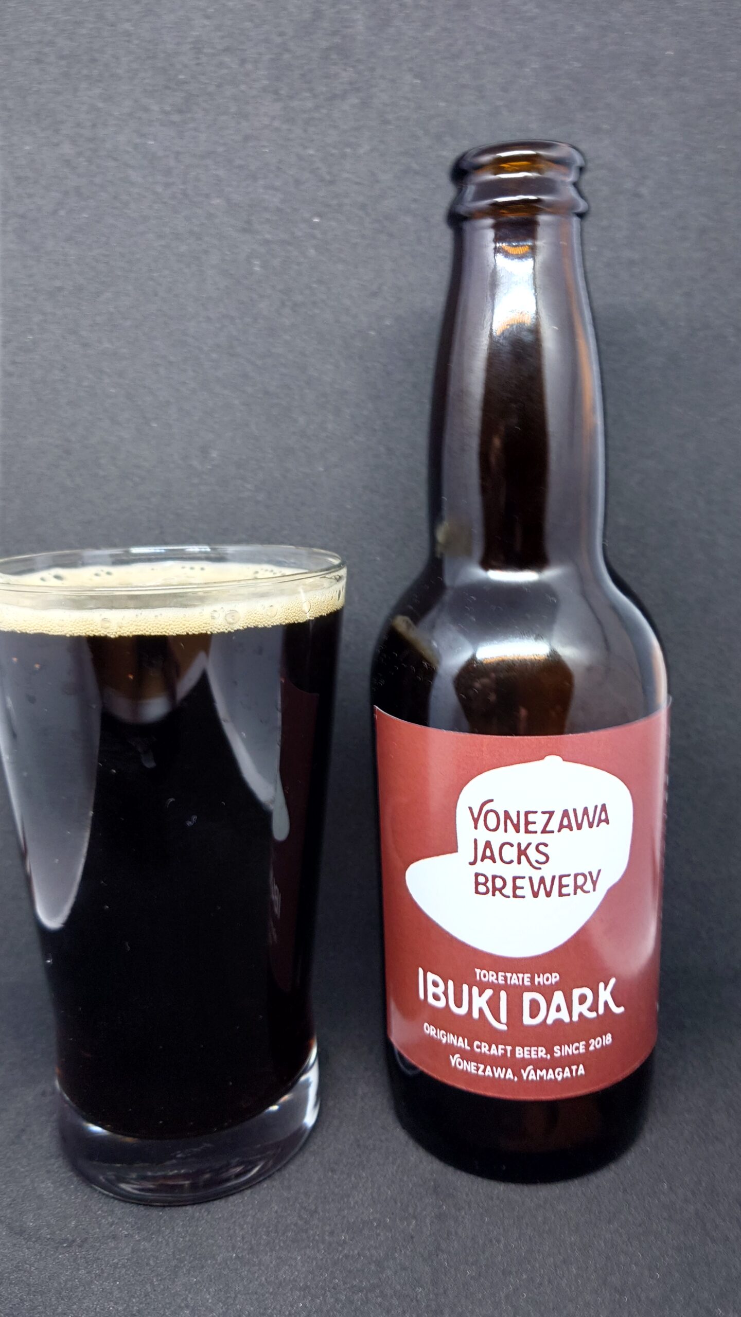 イブキダークをグラスに注いだ写真。黒色のビールと薄いベージュの泡、隣にイブキダークのボトルが置かれている。